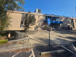 Clear blue sky over a beige brick building with a handicap parking sign and stone planter in front.