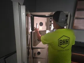 Worker in bright yellow shirt opening a large beige safe with multiple compartments in a dimly lit room.