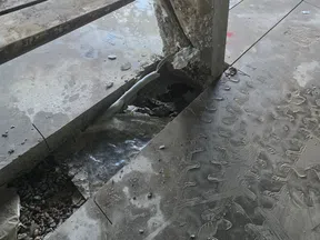 Damaged concrete floor with exposed gravel, broken pipe, and corroded metal framework in construction site.