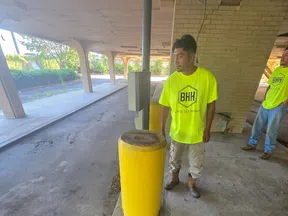 Two workers in bright yellow BHH Land Clearing shirts standing near a yellow bollard under a covered structure.