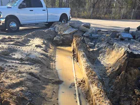 Construction site trench filled with muddy water and a pipe, white truck parked nearby under sunlight.
