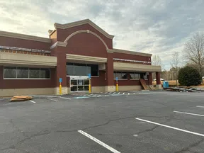 Vacant brick commercial building with empty parking lot and scattered debris under cloudy sky