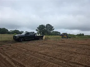 Black pickup truck and compact loader parked on a freshly tilled dirt field under cloudy sky