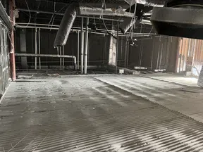 Interior view of an unfinished building ceiling showing ductwork, pipes, and exposed metal framework.