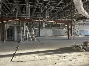 Interior of a large industrial space under renovation with exposed beams, pipes, and construction equipment.