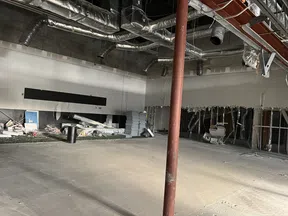 Interior of a commercial building under renovation with exposed ducts and construction materials scattered.