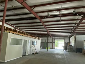Spacious empty industrial warehouse interior with metal beams, concrete floor, and small office room inside.