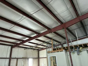 Interior of an industrial warehouse with exposed steel beams and unfinished walls and ceiling panels.