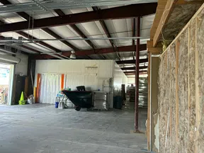 Interior view of an industrial warehouse with exposed beams, insulation, and storage containers.