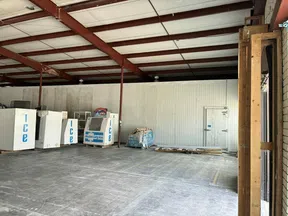 Empty industrial warehouse area with ice vending machines against a corrugated metal wall and concrete floor.
