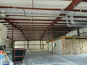 Interior of a large industrial warehouse with exposed ceiling beams, concrete floor, and construction materials inside.
