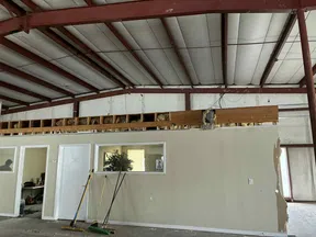 Interior of a building under renovation with exposed ceiling beams, a white partition wall, and cleaning tools.