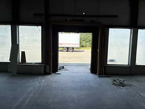 Empty warehouse interior with large door open to parking lot and truck visible outside on sunny day