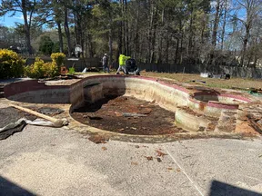 Empty, damaged backyard swimming pool undergoing cleanout and repair with workers and equipment nearby.
