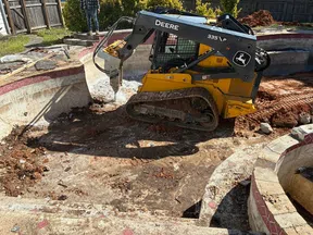 Yellow John Deere 335VP skid steer excavator working inside an empty backyard pool under renovation during daytime.