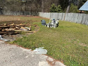 Backyard with a pool pump system, scattered wood, grassy area, fenced with trees and solar panel roof visible.