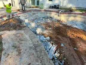 Demolition of an old backyard pool with debris and workers breaking concrete around the pool area.