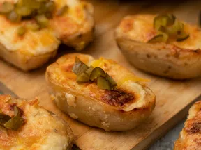 Close-up of twice-baked potatoes topped with melted cheese and chopped pickles on a wooden board.