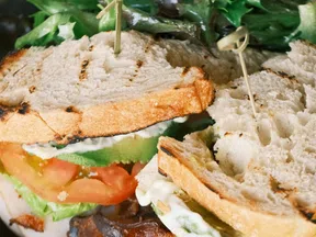 Close-up of a sandwich with grilled bread, lettuce, tomato, bacon, and mayonnaise on a plate.