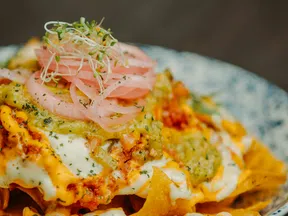 Plate of loaded nachos topped with melted cheese, guacamole, sour cream, pickled onions, and microgreens.