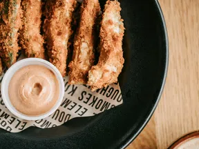 Crispy breaded chicken tenders served with a creamy dipping sauce on a black plate.