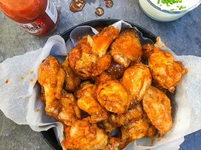 Spicy buffalo chicken wings served with a bottle of hot sauce and a glass of creamy dipping sauce topped with chives.