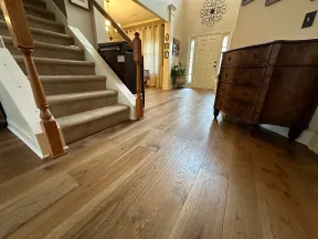 Spacious home entry with light oak hardwood flooring, carpeted stairs, and wooden chest next to front door.