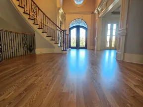 Spacious foyer with polished hardwood floors, ornate staircase, wrought iron railing, and large decorative front doors.