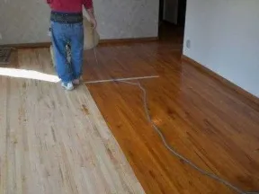 Person refinishing a hardwood floor showing contrast between sanded light wood and finished darker wood.