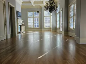 Spacious empty living room with hardwood floors, large windows, chandelier, and coffered ceiling in natural light.