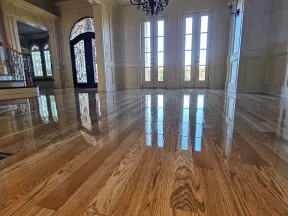 Shiny polished hardwood floors in a spacious elegant room with white walls, large windows, and a black chandelier.