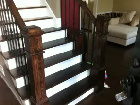 Dark wood staircase with white risers, black iron spindles, and a beige sofa in the background living room