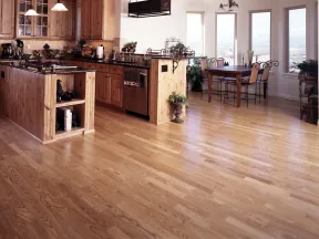 Spacious kitchen and dining area with wooden floors, wooden cabinets, black countertops, and large windows with a view.