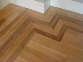 Close-up of a corner with a chevron oak wood floor pattern in varying natural wood tones.