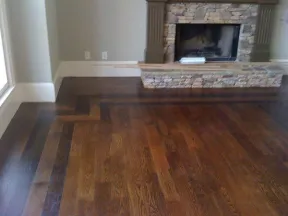 Rich hardwood flooring with dark border detail in front of a stone fireplace in a cozy living room.