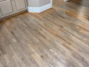 Clean kitchen corner with wooden floors, beige cabinetry, stainless steel microwave, and light beige walls.