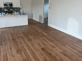 Modern kitchen with white cabinetry, gray backsplash, and new wood grain laminate flooring in an open space.