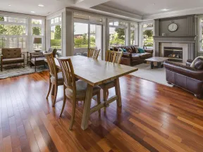 Bright open dining and living room with wooden floors, large windows, fireplace, and modern furniture.