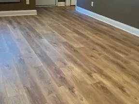 New wood-effect vinyl plank flooring installed in an empty room with beige walls and white baseboards.