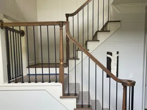 Interior view of a wooden staircase with black iron balusters and beige carpeted steps in a modern home.