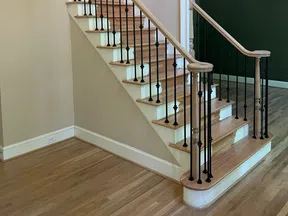 Wooden staircase with black metal balusters and light hardwood flooring in a neutral-toned room.