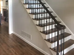 Wooden staircase with dark metal balusters and hardwood flooring in a modern home interior.