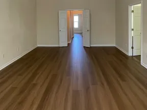 Empty room with wood flooring, beige walls, white trim, and open doorways leading to a hallway and adjoining room.