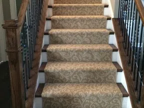 Upholstered staircase with beige patterned carpet runner and dark wood handrails and spindles in a home.