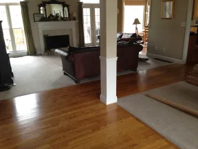 Open living room with hardwood and carpet flooring, leather couches, fireplace, and large windows with green curtains