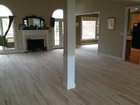 Spacious living room with light hardwood floors, white fireplace, large windows, and beige walls.