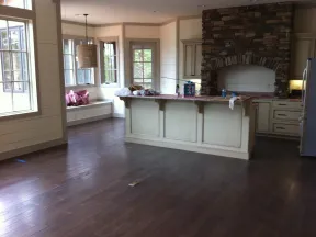 Spacious kitchen with dark wooden floor, cream island, stone fireplace, large windows, and window seat.