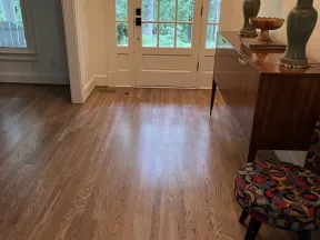 Entryway with wooden floor, glass-paneled door, retro chair, and wooden sideboard with lamps and décor.