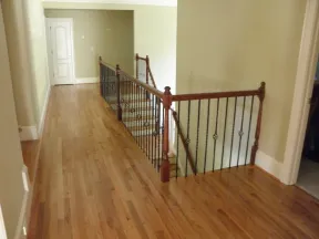 Wooden floor hallway with black metal and wood railing beside staircase and closed white door at end.