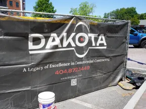 Black Dakota construction banner on chain link fence with commercial contracting contact info outdoors.